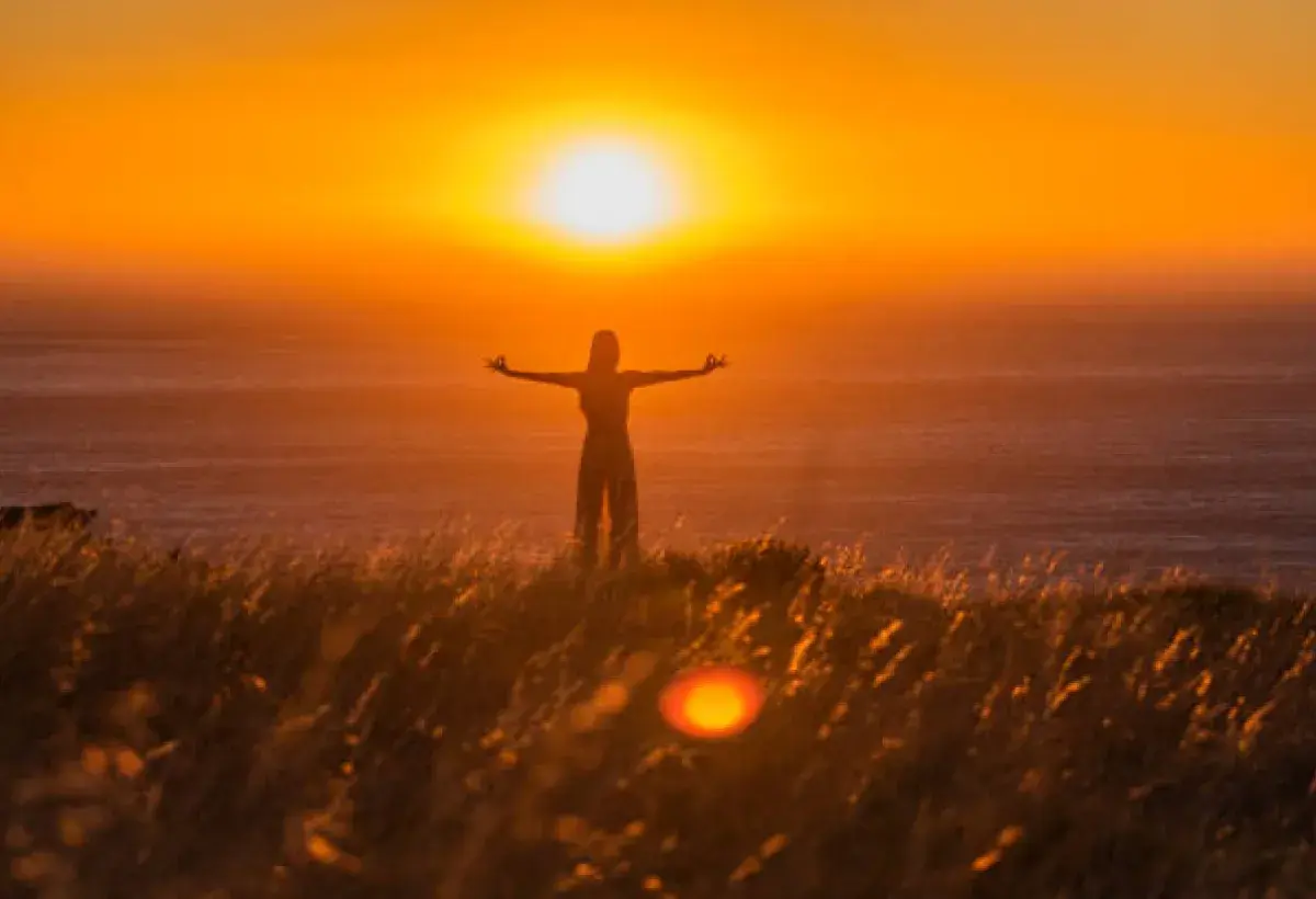 Person standing in a vast open field at sunset, symbolizing mindfulness and surrender