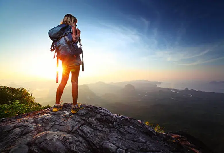 Person standing on a mountaintop at sunrise symbolizing the pursuit of happiness.