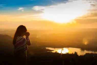 Hands lifted in prayer toward sunrise representing surrender to God