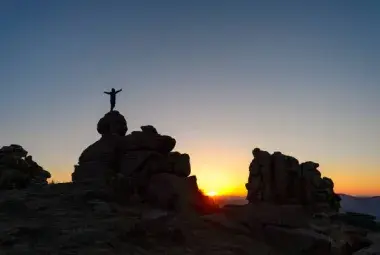 A person standing on a mountain peak at sunrise, representing perseverance and victory after struggle.